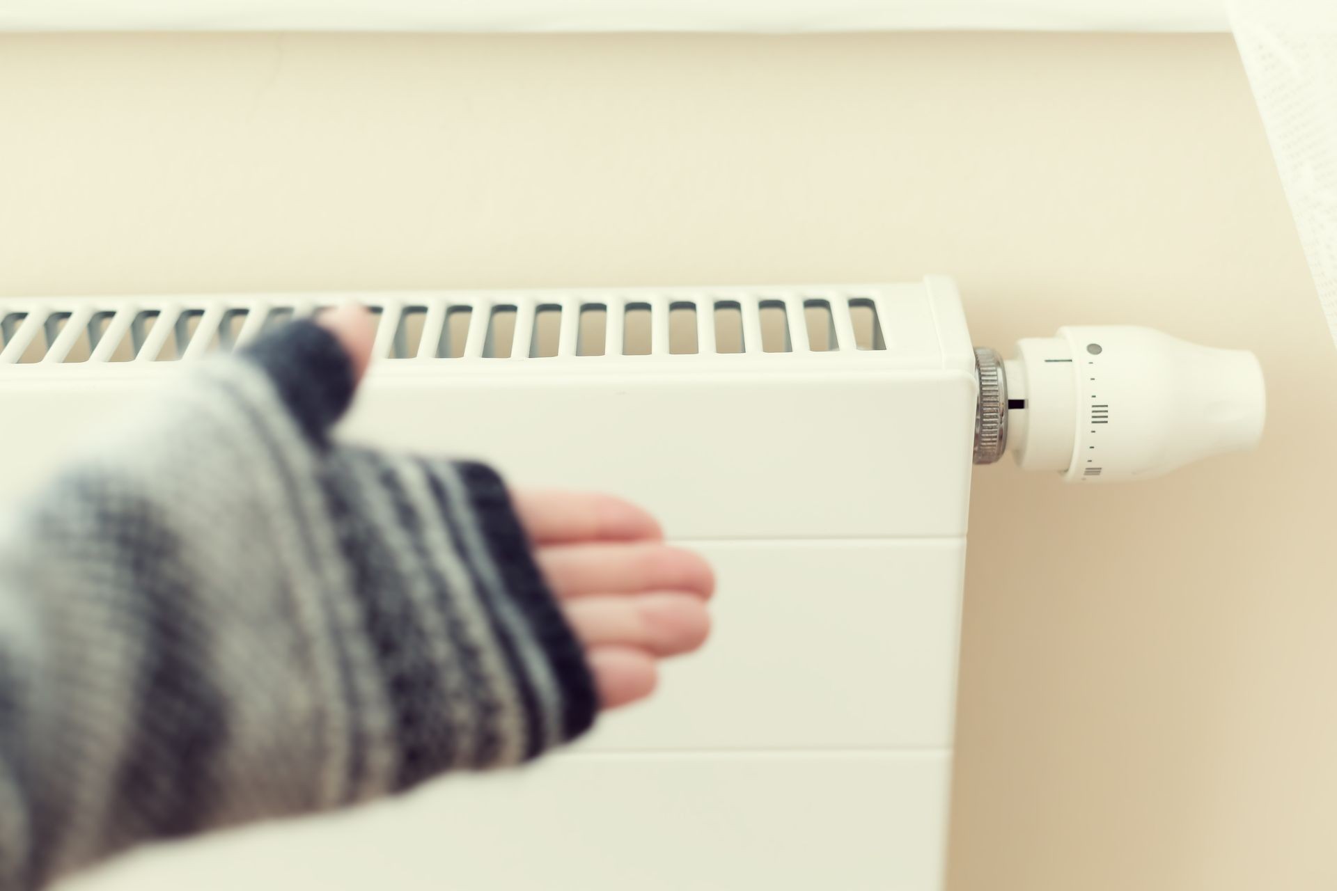 Hand in mittens regulate white heating radiator with a thermostat inside at home at cold season.